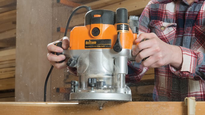 Oberfräse Triton präzise Holzfräsen, Hände halten Gerät, Arbeitsplatz Holzwerkstatt. Sautershop.